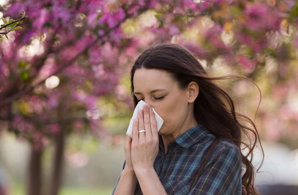 A woman wipes her nose with a tissue - sneezing and watery eyes can be a symptoms of allergies