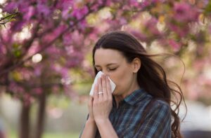 A woman wipes her nose with a tissue - sneezing and watery eyes can be a symptoms of allergies