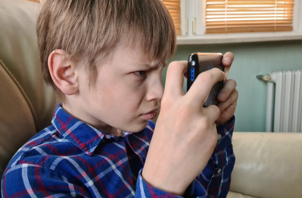 A young boy squinting and holding a smartphone close to his face while using it.