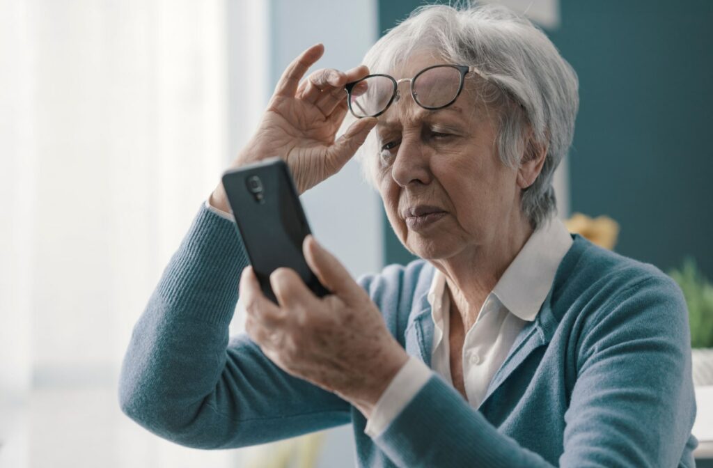 A senior woman adjusting her glasses and holding her phone closer to see its content clearer.