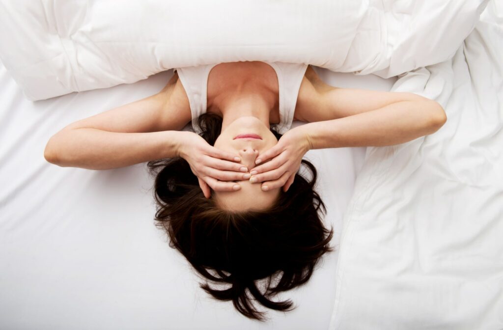 A woman lying in bed with her hands over her eyes as she's waking up