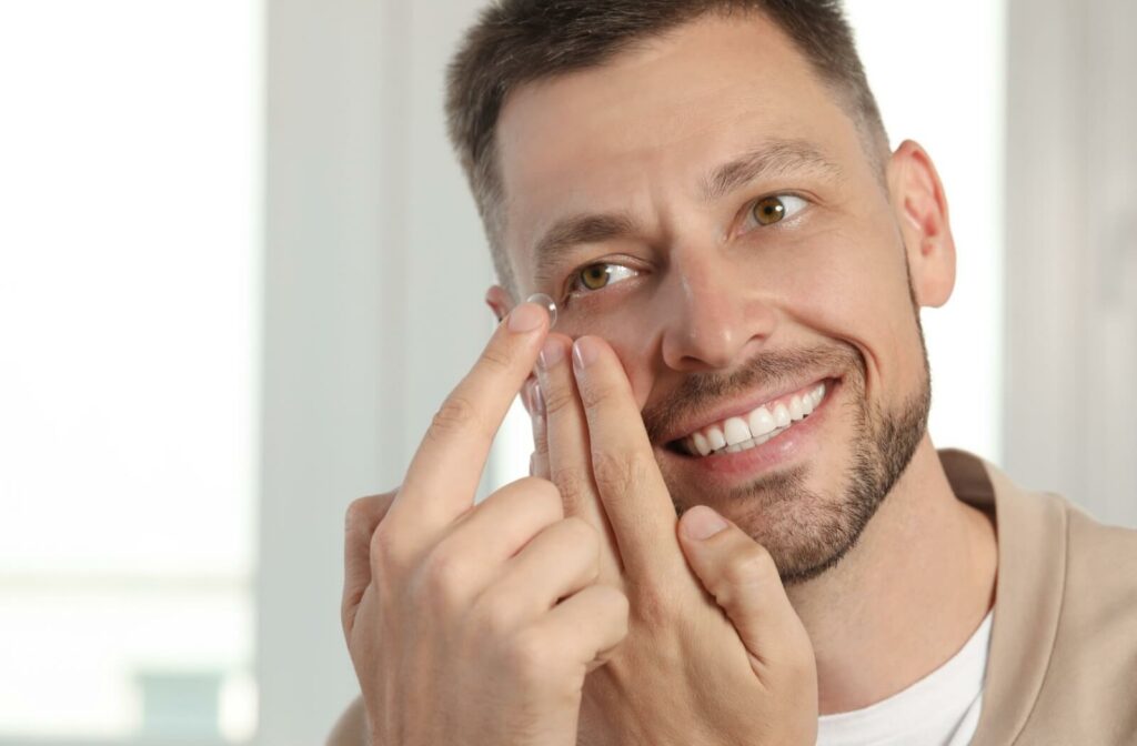 A man smiles as he inserts a contact lens into his right eye.