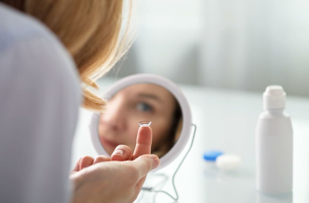 A woman sits in front of a small mirror, ready to put in her contact lens.