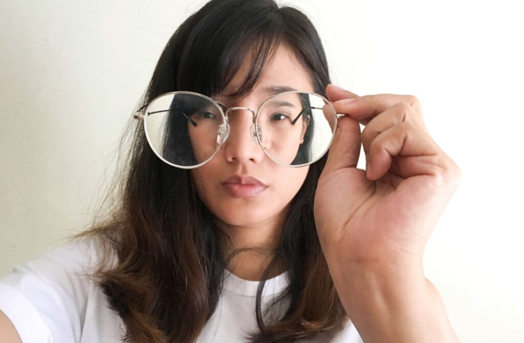 An adult holds a pair of circular eyeglasses in front of their face, causing their face to look distorted behind the lenses.