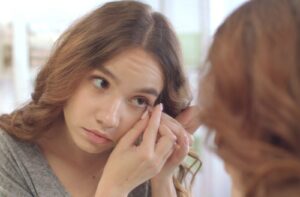 A close-up image of a person trying to remove a stuck contact lens in their mirror at home.