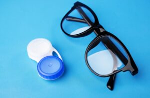 A pair of glasses and a contact lens case sit next to each other.