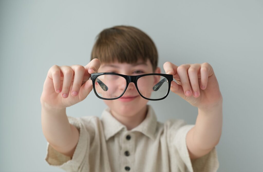 A blurry young child holds out their glasses into focus.