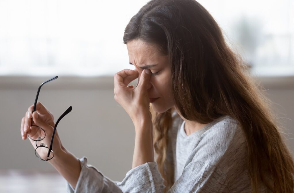 Woman with eye discomfort holding glasses, possibly experiencing dry eye symptoms.